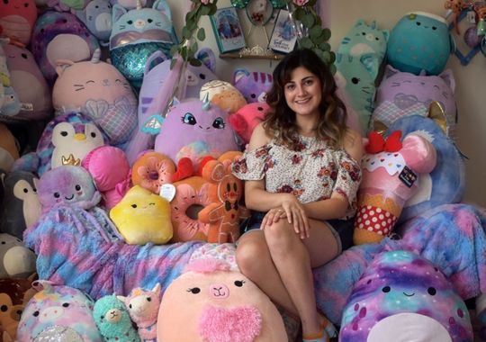 A woman seated on a couch with Squishmallows.