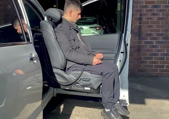 A man seated in a swivel car seat.