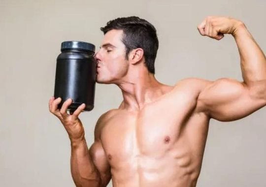 A muscular man with a bottle of pre workout supplement.