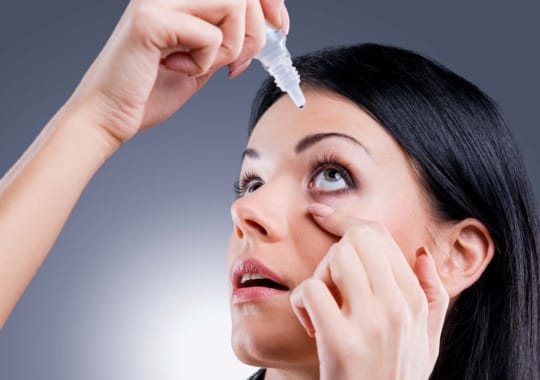 A woman putting eye drops in the eyes.