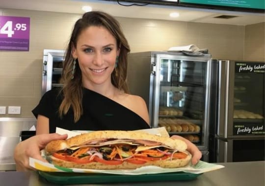 A woman holding a subway sandwich.