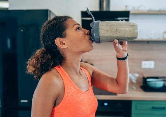 A woman drinking a bottle of protein shake.
