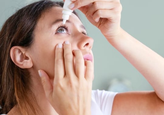 A woman putting eye drops in the eyes.