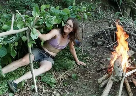 A woman making a shelter in the woods.