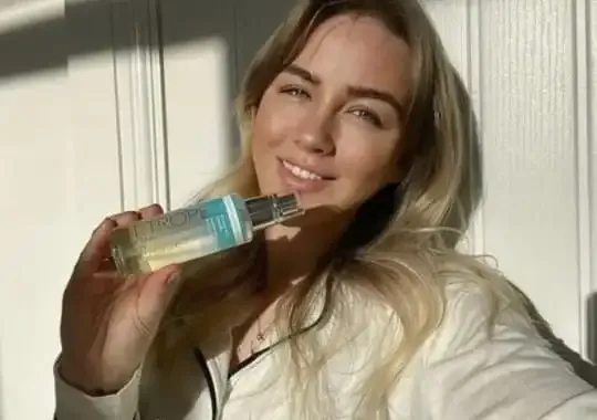 A woman holding a bottle for facial cleansing after a spray tan.