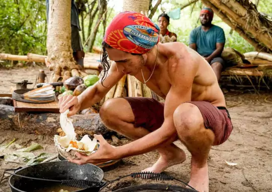 A man in the woods helping himself serve food.
