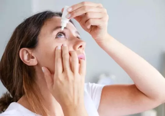 A woman applying eye drops in the eyes.