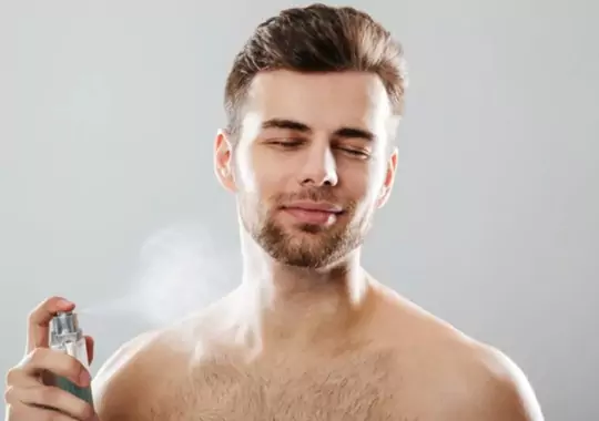 A man spraying himself perfume.