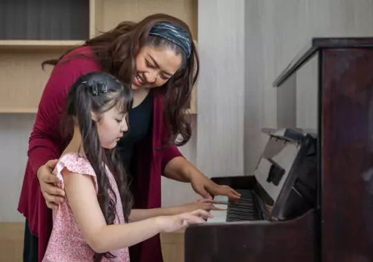 A woman teaching a little girl how to play piano.