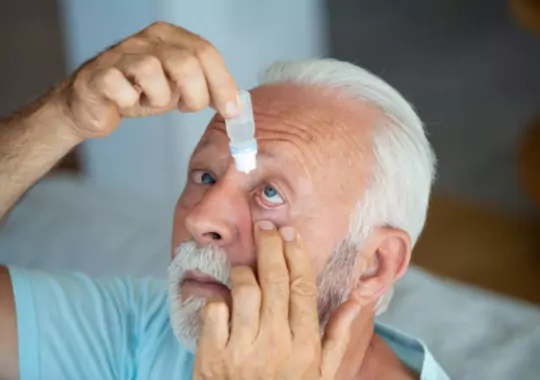 An old man applying eyedrops in the eyes.