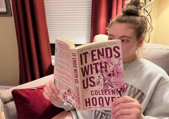 A woman reading a colleen hoover book.