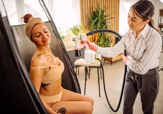 A woman being sprayed with a spray tan after showering.